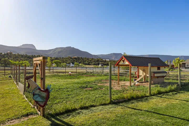 Expansive fenced pasture featuring a well-maintained chicken coop with a metal roof, an integrated roosting area, and an enclosed run