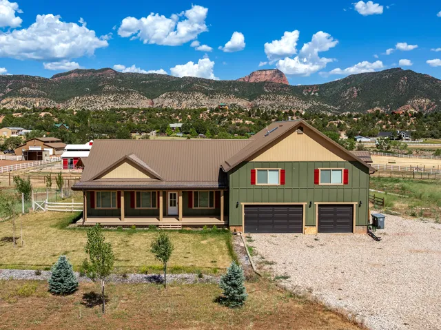 Ranch-style exterior with a mountain backdrop, featuring a covered front porch, two-car garage, and a gravel driveway