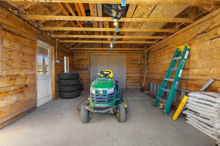Wood-paneled outbuilding with exposed ceiling joists, concrete flooring, and multiple light fixtures