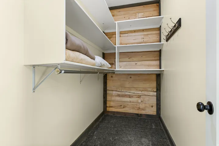 Built-in closet system featuring white shelving, a hanging rod, and a rustic wood panel accent wall