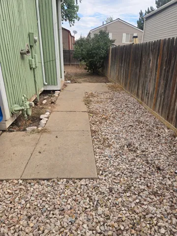 Concrete pathway alongside a wood-paneled exterior, featuring a gravel border and a wooden privacy fence