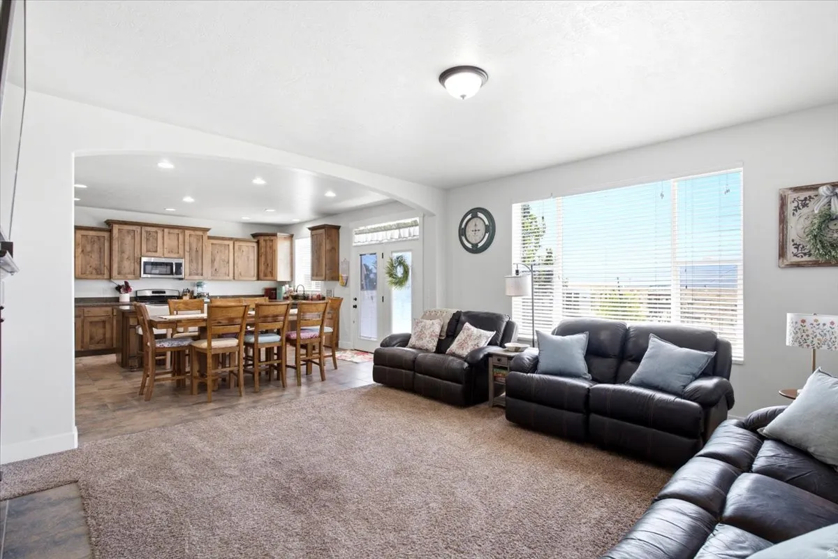 Expansive living area with carpet flooring and large windows, opening to a kitchen featuring wood cabinetry, stainless steel appliances, and a central island with seating