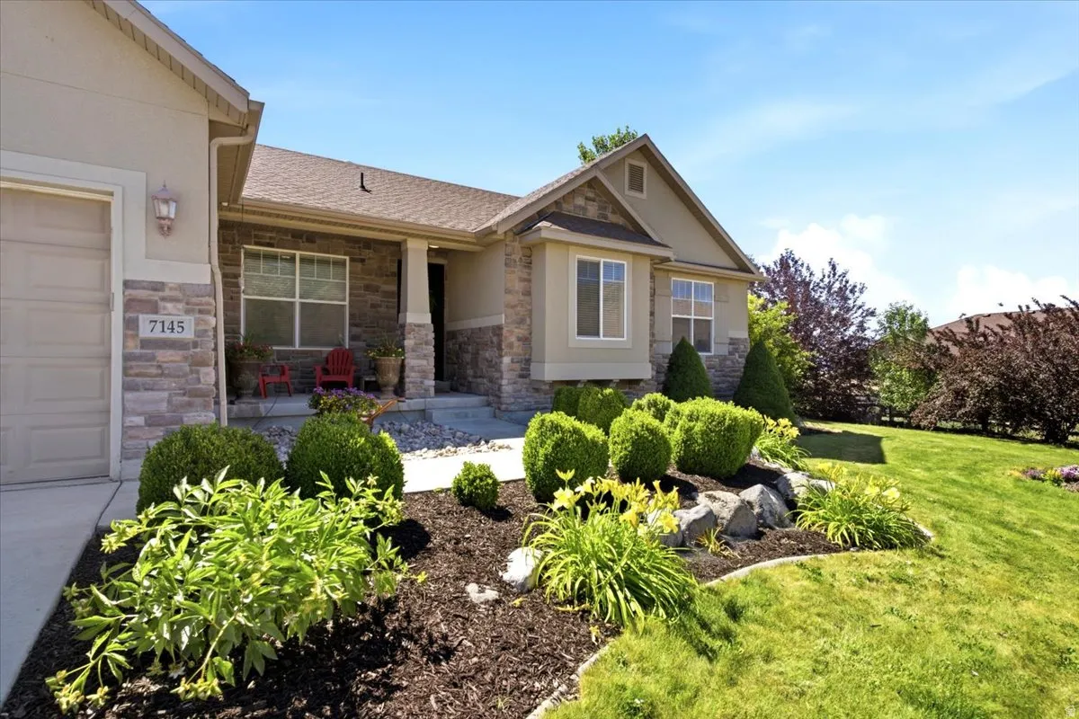 Stone and stucco exterior featuring a covered front porch, an integrated garage, a bay window, and a landscaped front yard with mature shrubbery