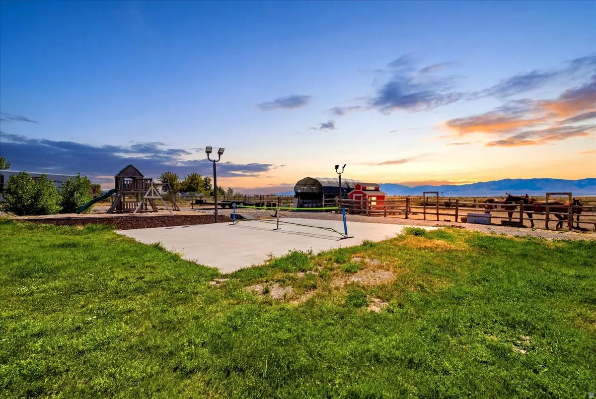 Expansive outdoor area featuring a concrete pad, a wooden play structure with slide, fenced animal enclosures, and a red barn structure