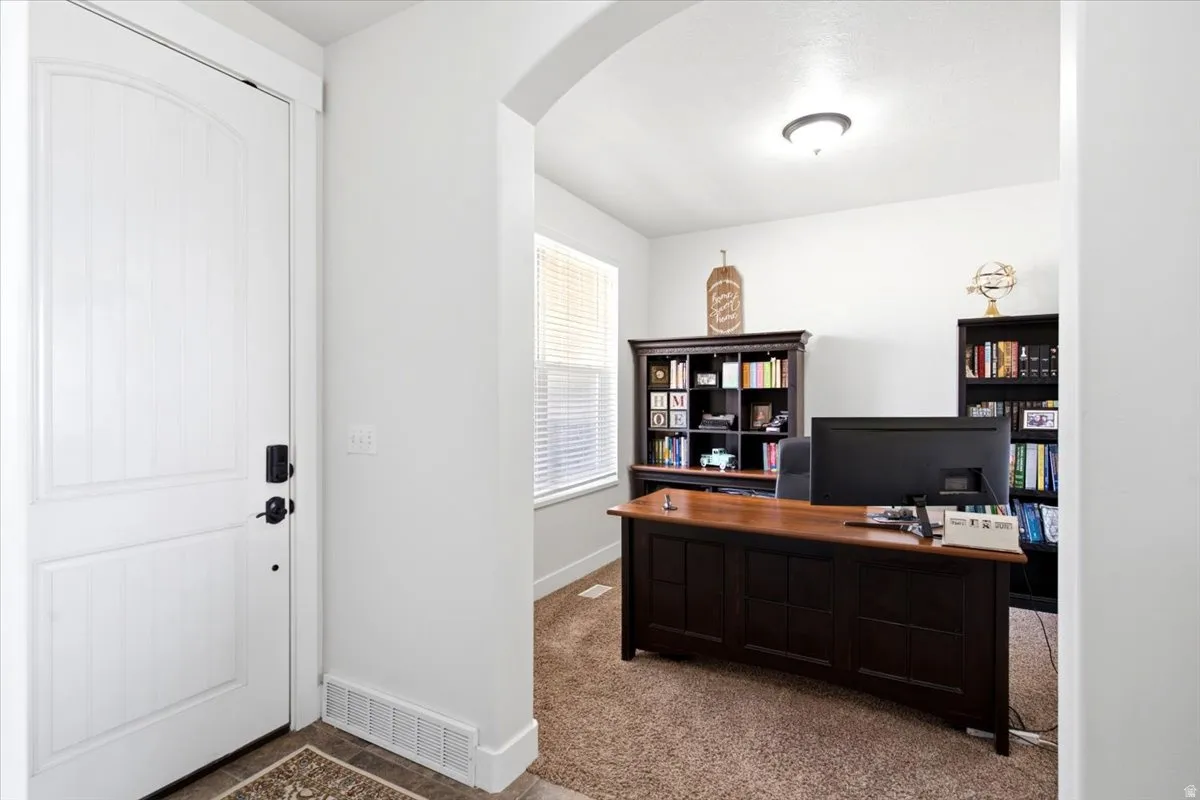 Dedicated office space featuring an arched entryway, neutral wall tones, and carpet flooring