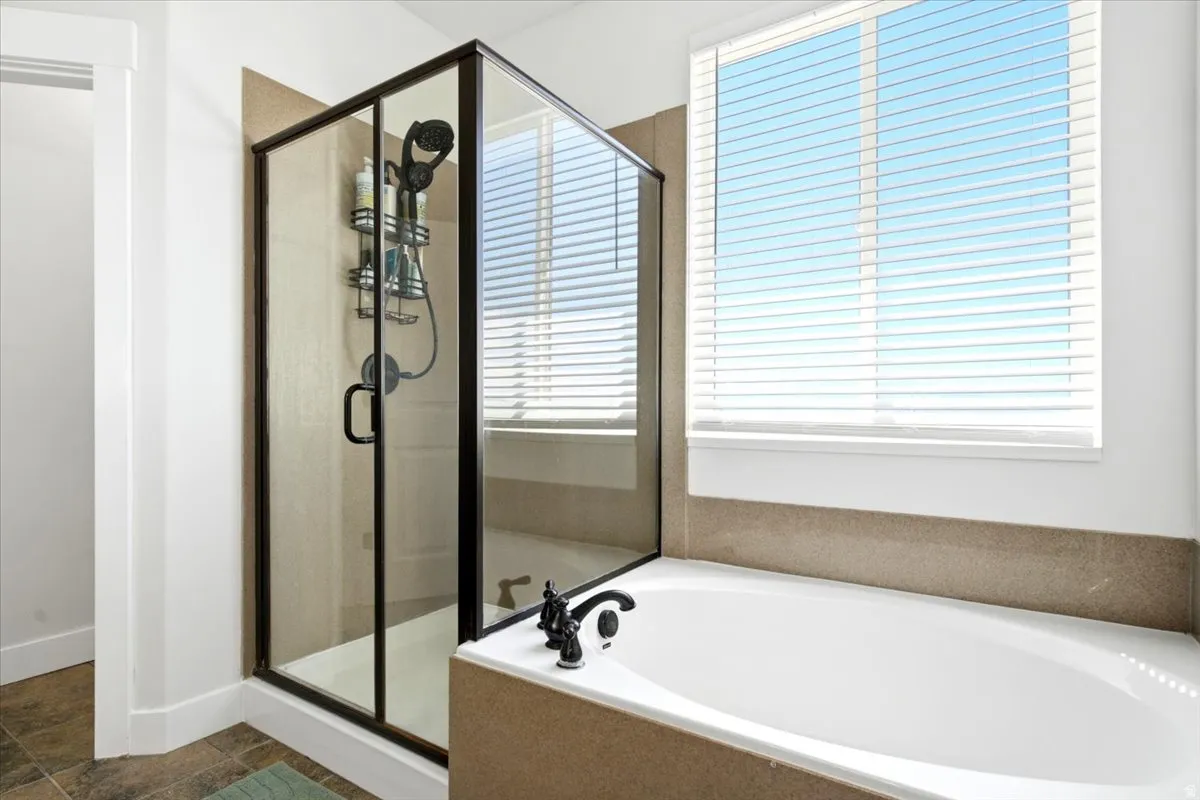 Bathroom featuring a built-in soaking tub, a glass-enclosed shower with a dark bronze frame, and a large window with horizontal blinds