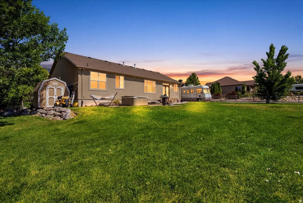 Expansive grassy yard with a storage shed, mature trees, and a stucco exterior