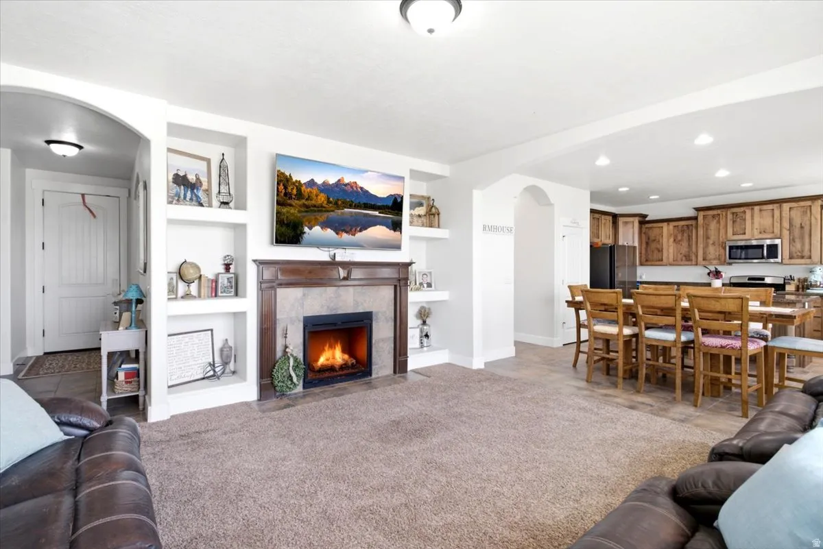 Living area featuring a fireplace with a wood mantle and stone surround, built-in shelving, and carpet flooring