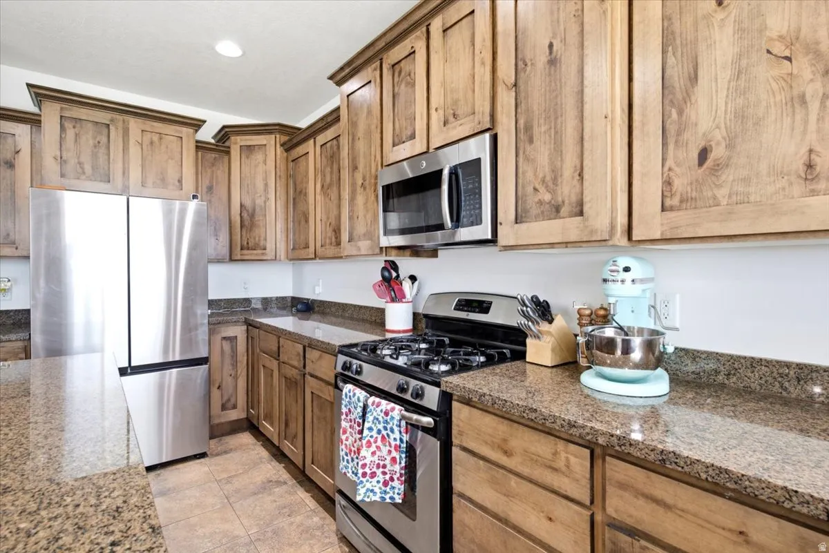 Kitchen featuring wood cabinetry, stainless steel appliances, speckled stone countertops, and tile flooring