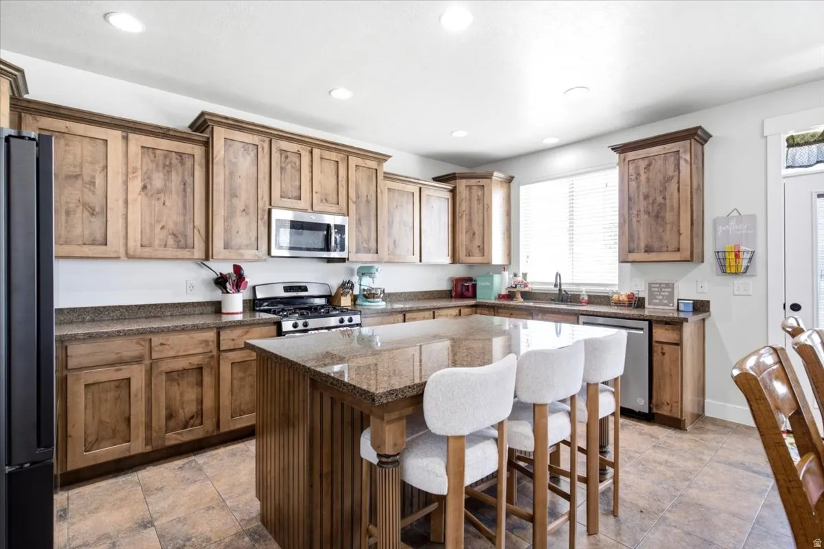 Kitchen featuring a large central island with seating, extensive wood cabinetry, stainless steel appliances, recessed ceiling lighting, and a window with blinds