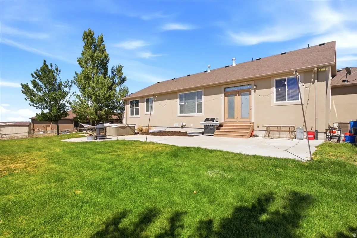 Expansive backyard featuring a large concrete patio, mature trees, a built-in hot tub, and a decorative fire pit area