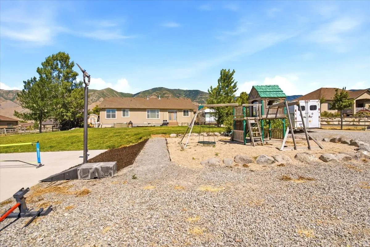 Expansive gravel and sand area featuring a wooden play structure with swings, slide, and ladder