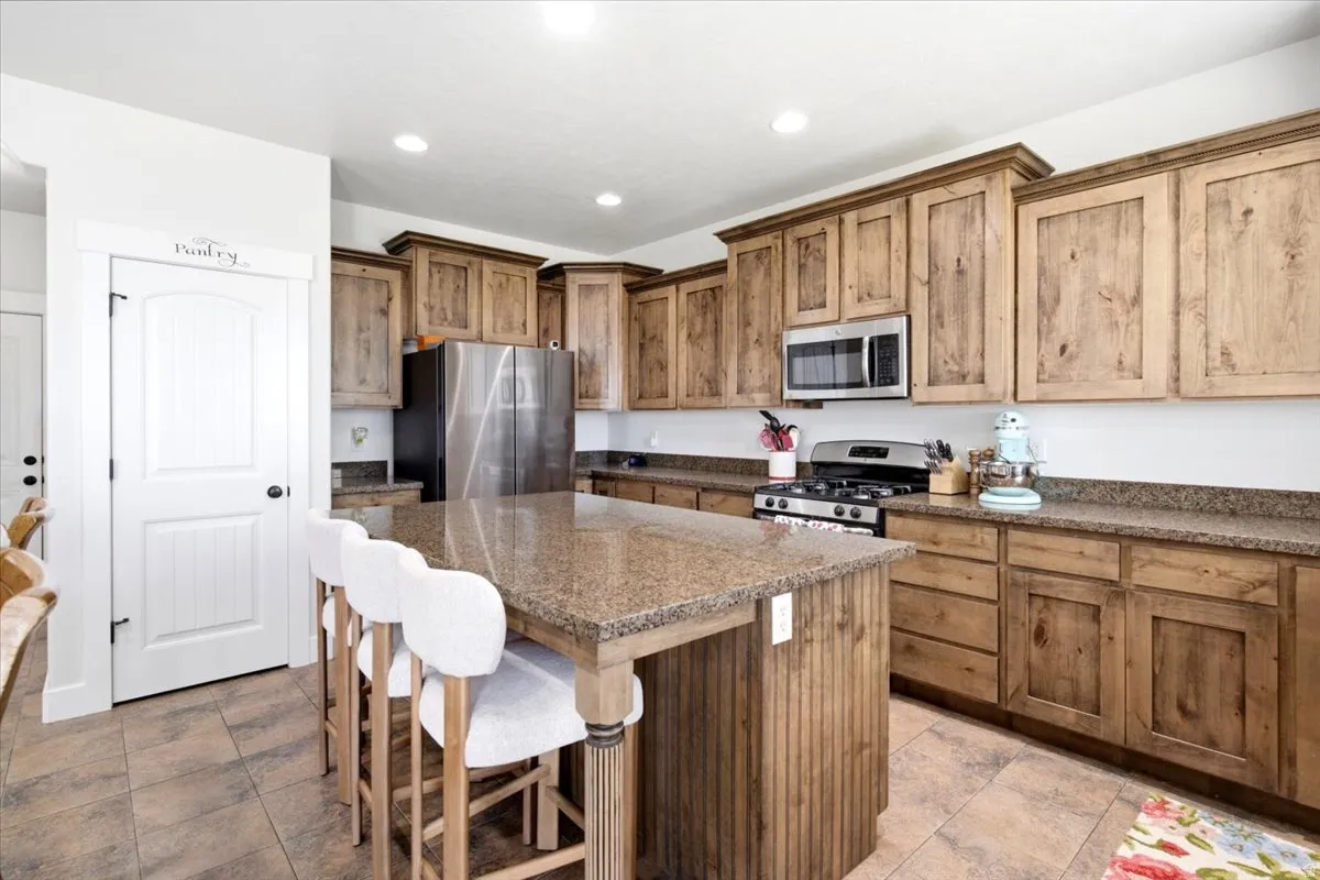 Open-concept kitchen featuring a central island with a granite-style countertop, recessed lighting, wood-finish cabinetry, stainless steel appliances, and tiled flooring