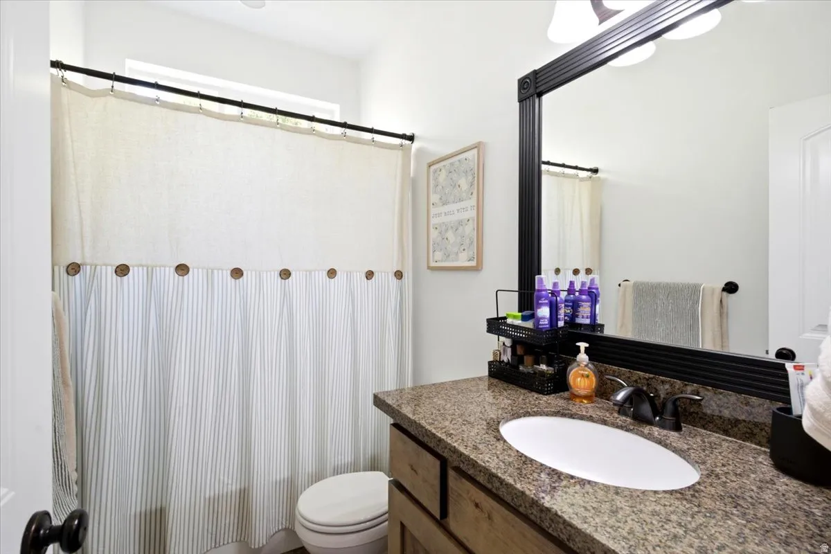 Bathroom featuring a brown granite countertop, oval undermount sink, and a dark wood-finish vanity