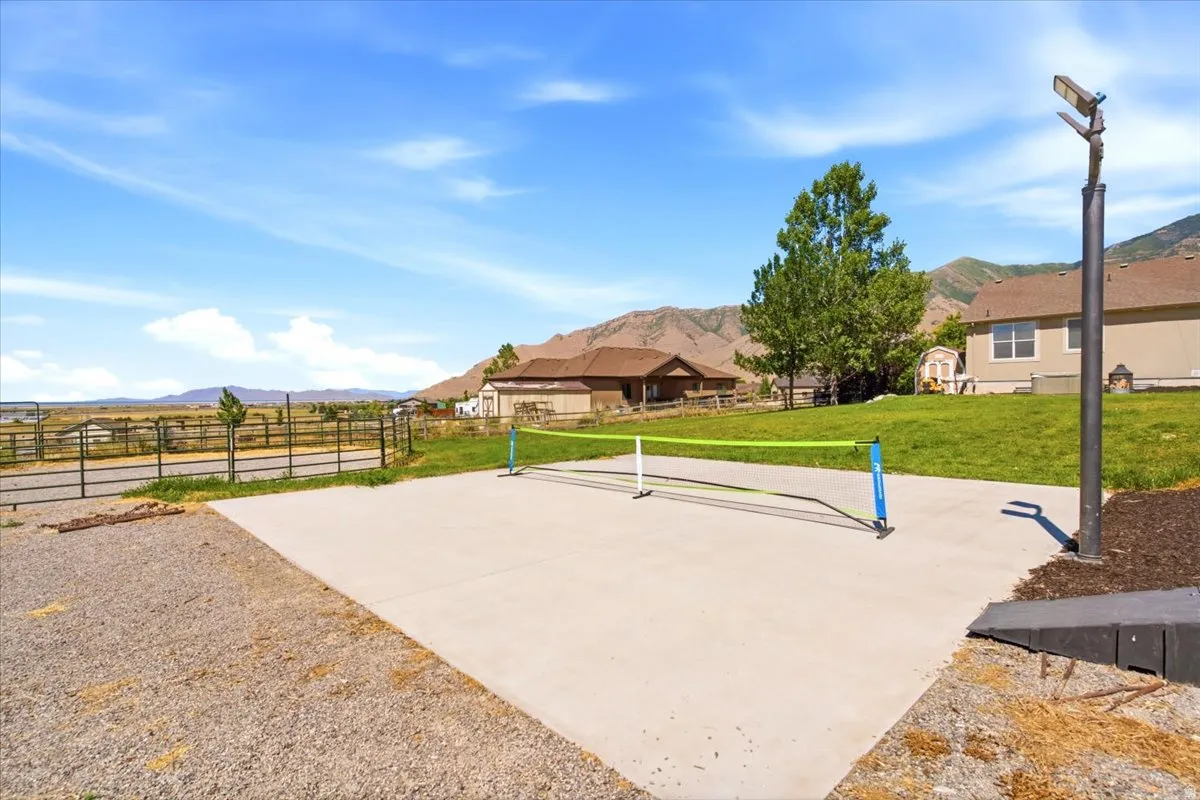 Concrete sport court area with an adjacent gravel pad, surrounded by a manicured lawn and a privacy fence