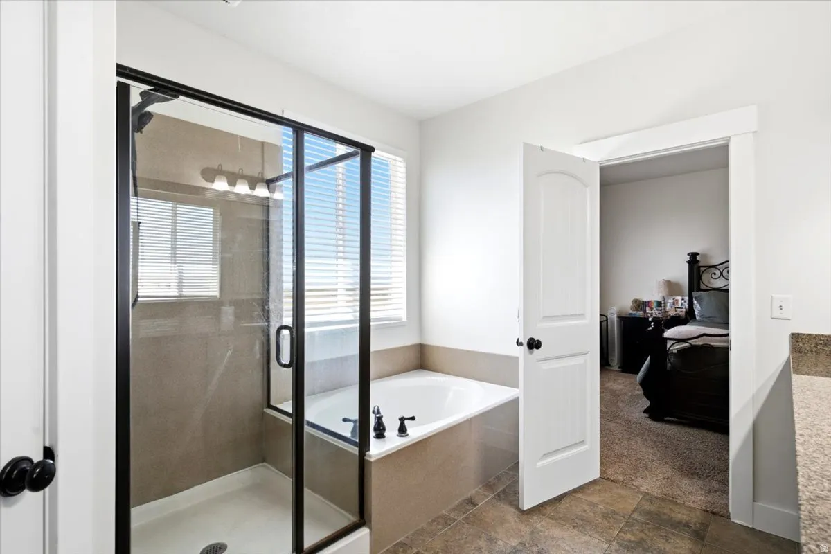 Shower-and-tub combination featuring a glass enclosure with black framing, a built-in soaking tub, and a window with blinds