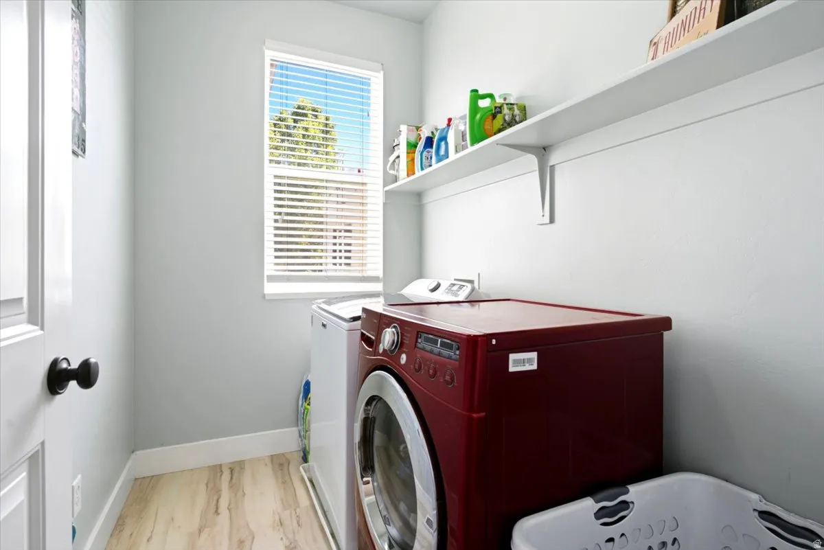 Laundry area featuring a window with blinds, overhead shelving, and wood-finish flooring