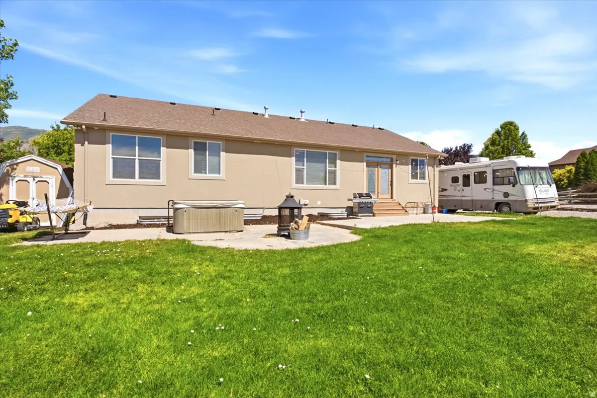Spacious backyard featuring a large green lawn, a ground-level patio with a spa, a freestanding shed, and a dedicated RV parking area
