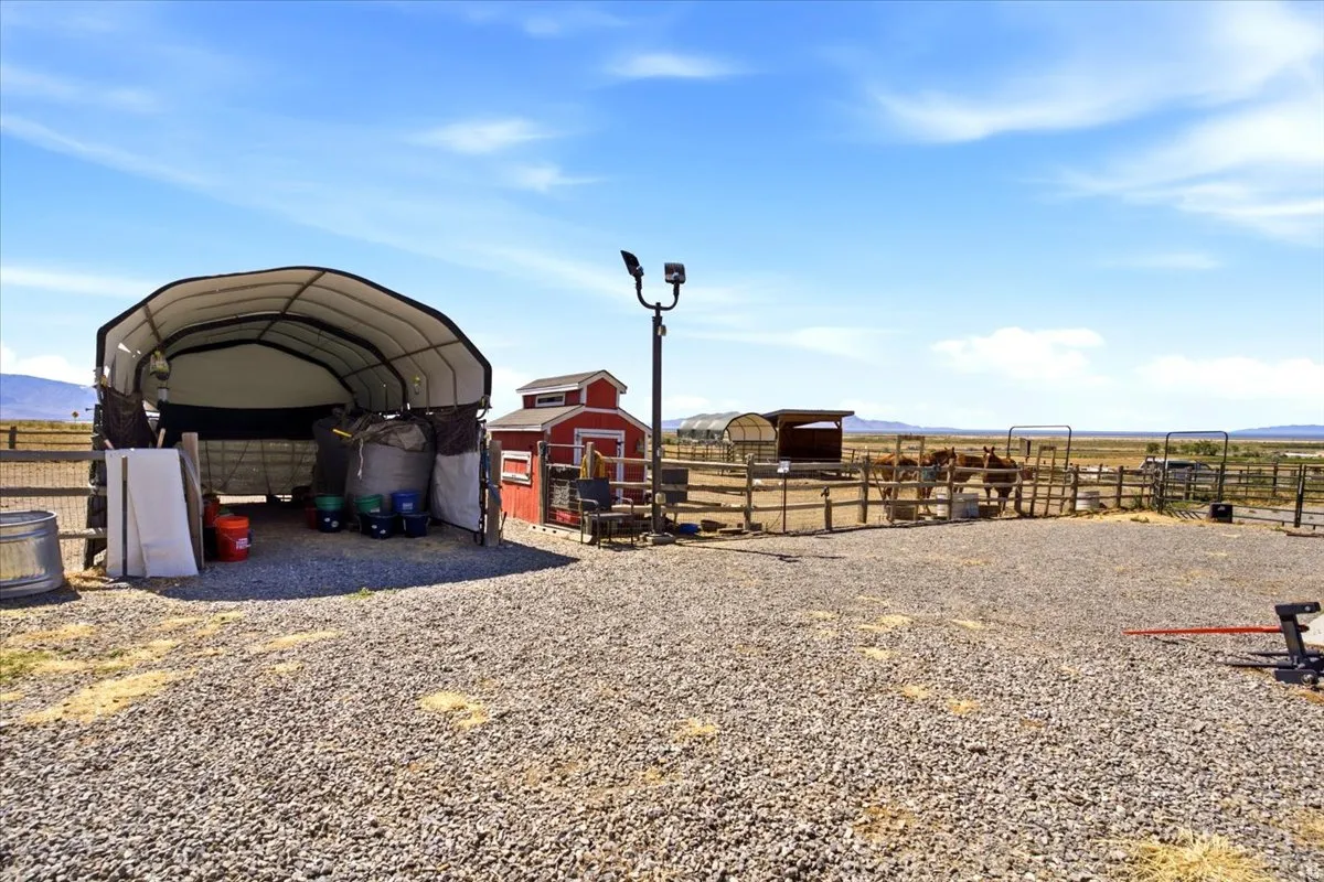 Expansive gravel area featuring a covered shelter, a red storage shed, and a fenced enclosure