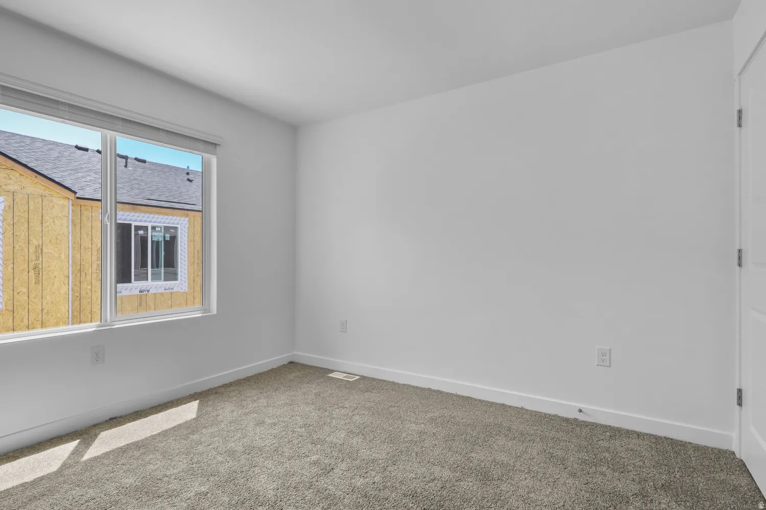 Neutral interior room featuring a large window, light gray carpet, white walls, and white trim