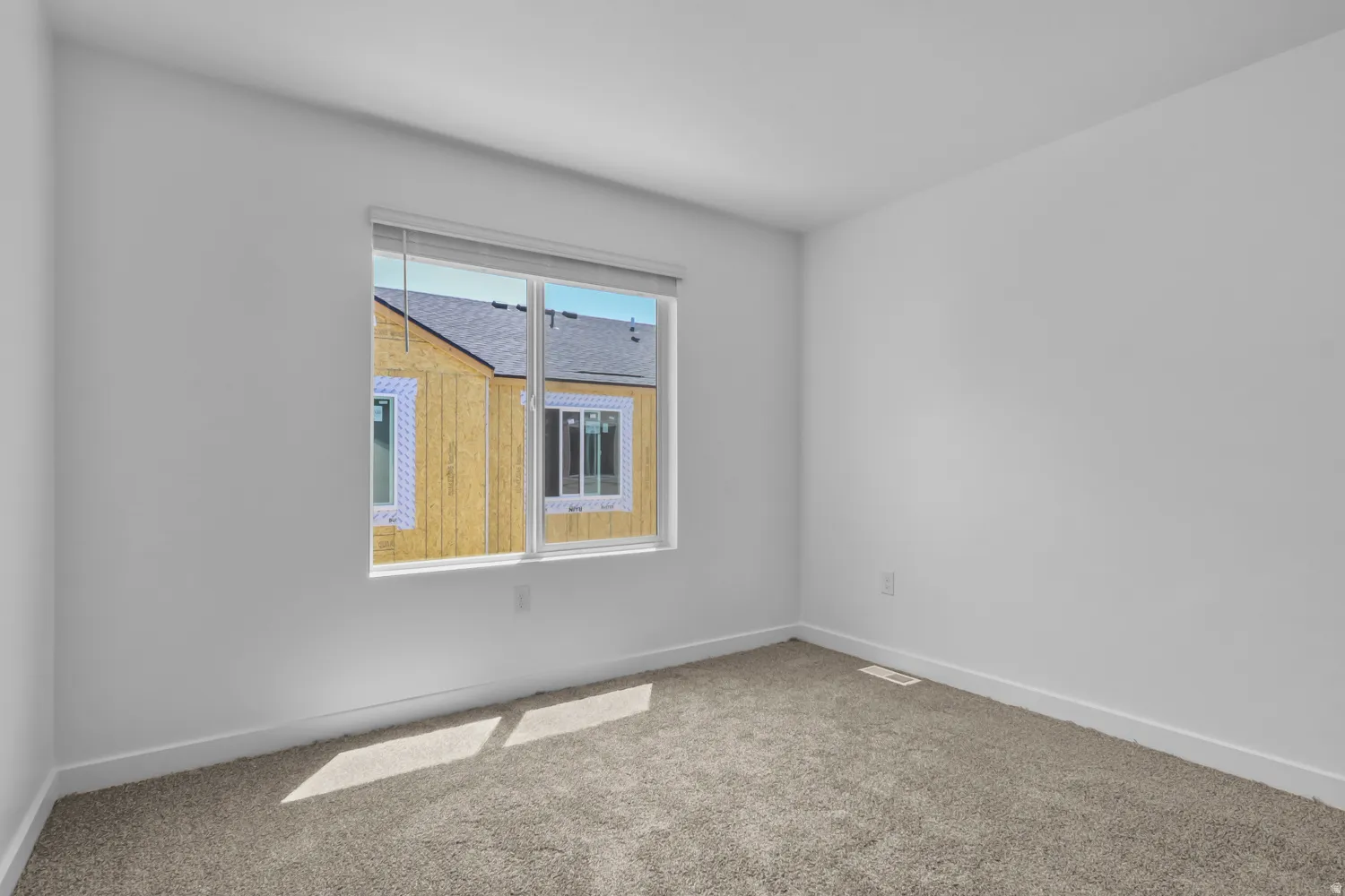 Bright interior space featuring a window with integrated blinds, neutral carpeting, white baseboards, and freshly painted walls