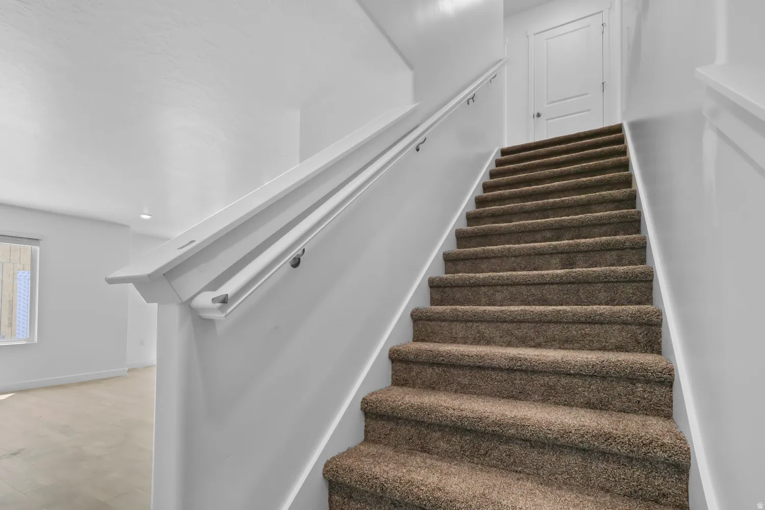 Carpeted staircase with white handrails and trim, featuring a contemporary paneled door at the landing