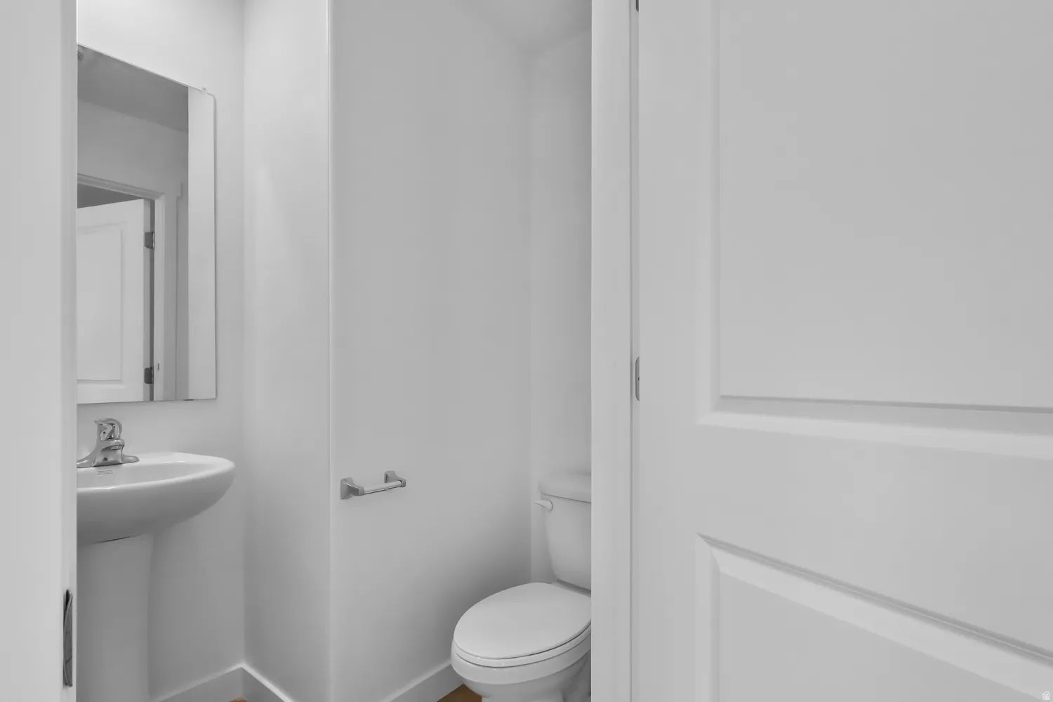 Powder room featuring a pedestal sink with chrome faucet, wall-mounted mirror, and a toilet