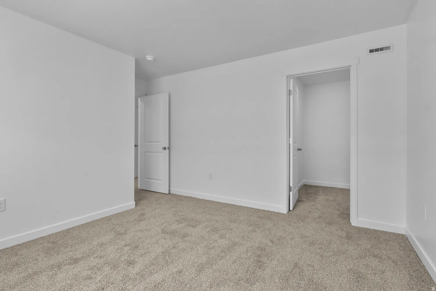 Carpeted room featuring white walls, white baseboards, and a white interior door with a silver handle