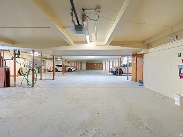 Spacious concrete-floored garage featuring exposed ceiling beams, fluorescent lighting, and a garage door opener system