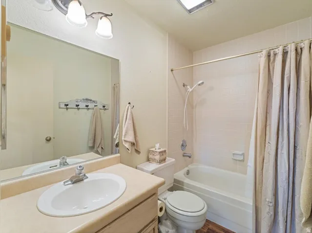 Full bathroom featuring a single-sink vanity with an oval basin, a combination shower and tub, and wood-finish flooring