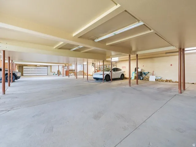 Expansive covered concrete parking area featuring multiple support columns, fluorescent overhead lighting, and a roll-up garage door
