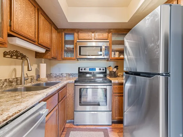 Kitchen featuring wood cabinetry, stainless steel appliances, a double basin sink with a gooseneck faucet, and stone countertops