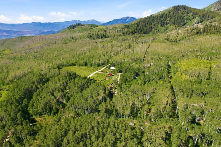 Expansive mountainous terrain featuring dense forests, open clearings, and distant mountain ranges