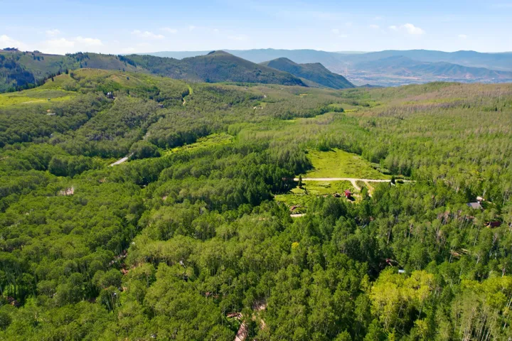 Extensive mountainous landscape featuring dense tree coverage, distant mountain ranges, and a clear expanse of sky