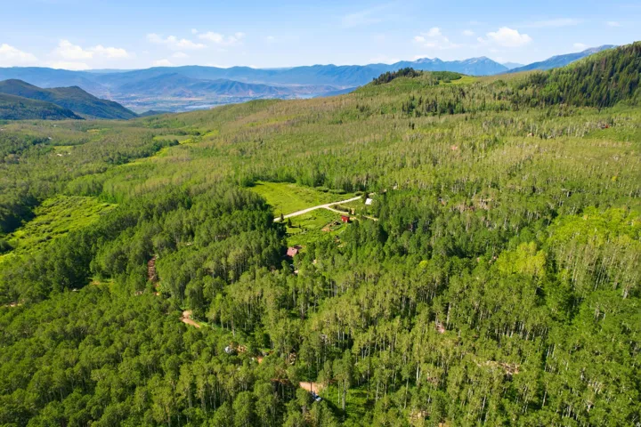 Expansive mountain landscape featuring dense green foliage, distant mountain ranges, and a partially visible structure among the trees