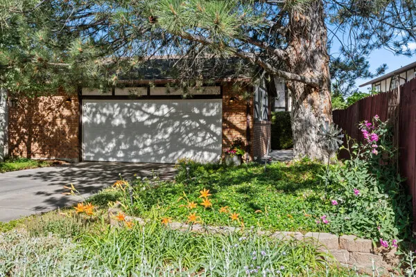 Front exterior featuring a two-car garage, brick facade, and mature landscaping with a variety of plantings
