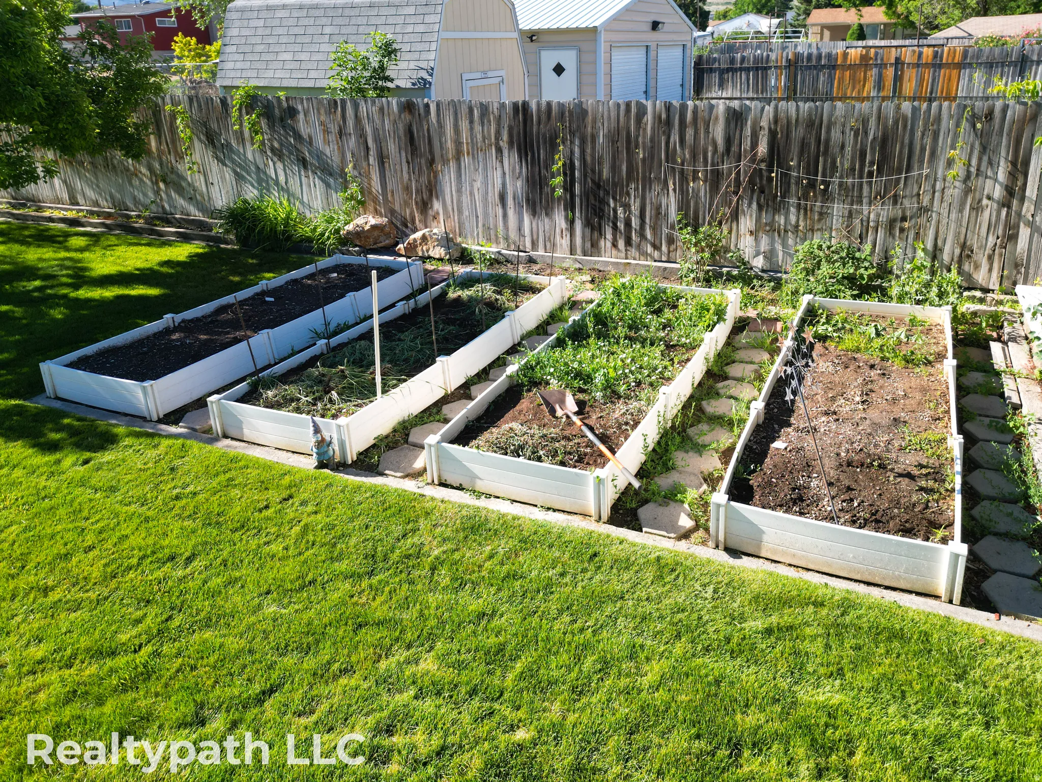 Expansive backyard featuring a manicured lawn, a wooden privacy fence, and four raised garden beds with stepping stones