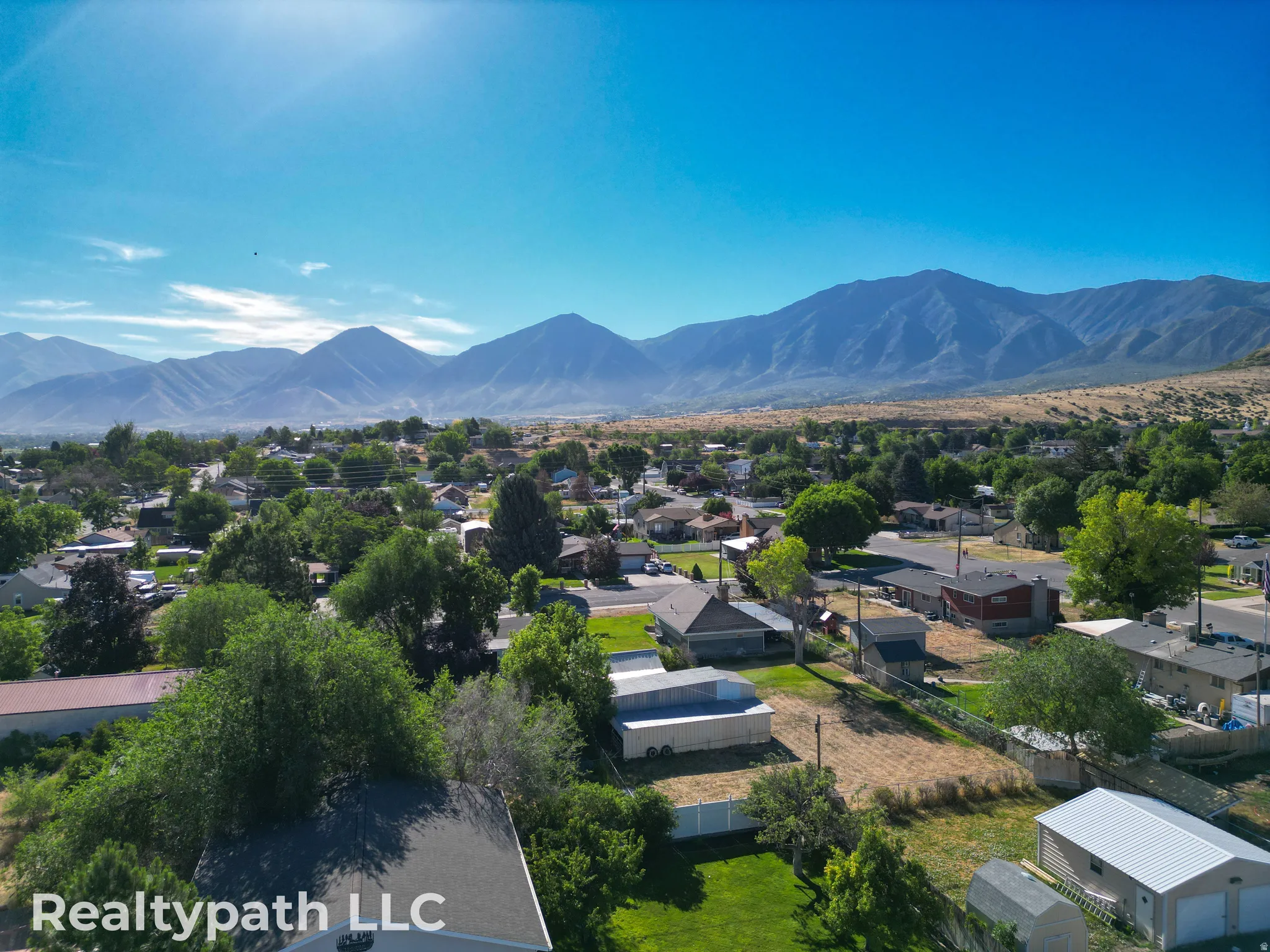 Expansive mountain backdrop with a residential neighborhood featuring numerous mature trees and a clear blue sky
