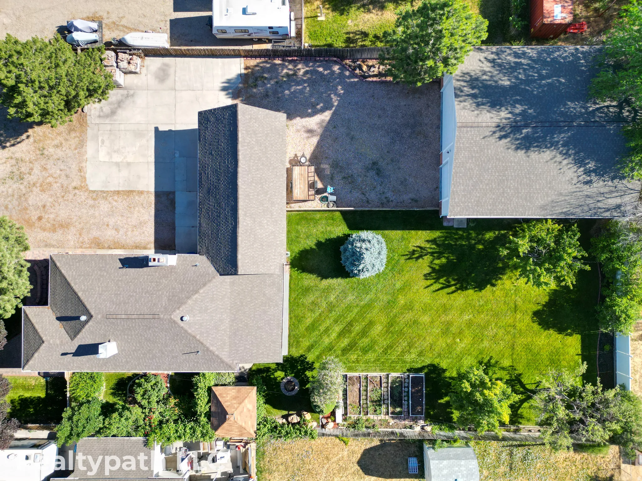 Expansive grassy yard area featuring a central evergreen shrub, mature trees, and raised garden beds