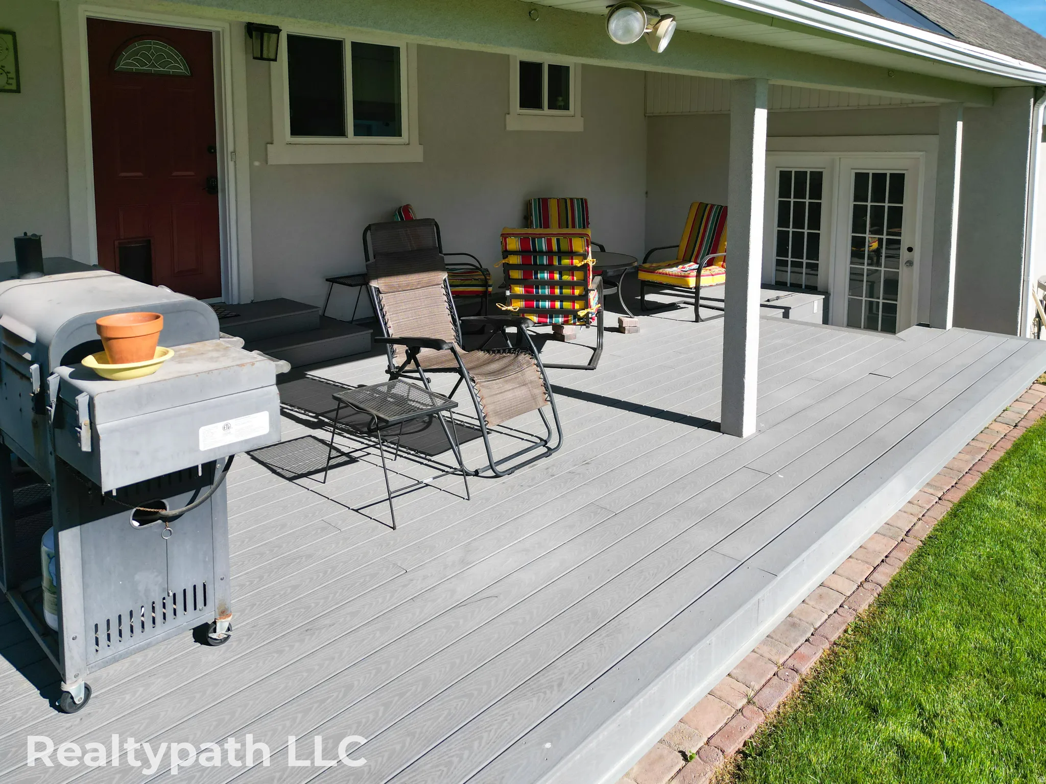 Spacious outdoor deck featuring gray composite decking, supporting columns, and a brick border