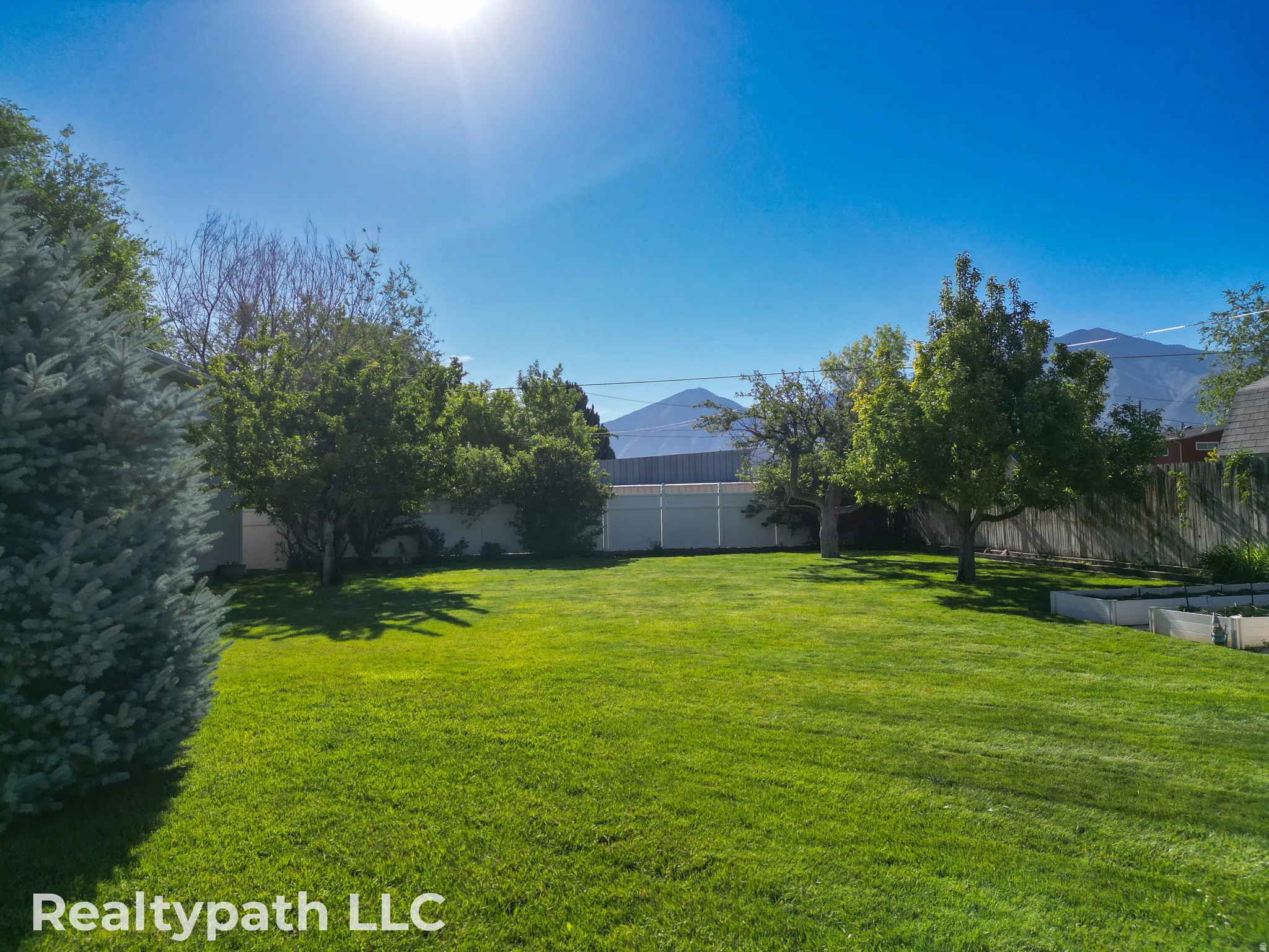 Expansive fenced backyard featuring a manicured lawn, mature trees, and mountain scenery