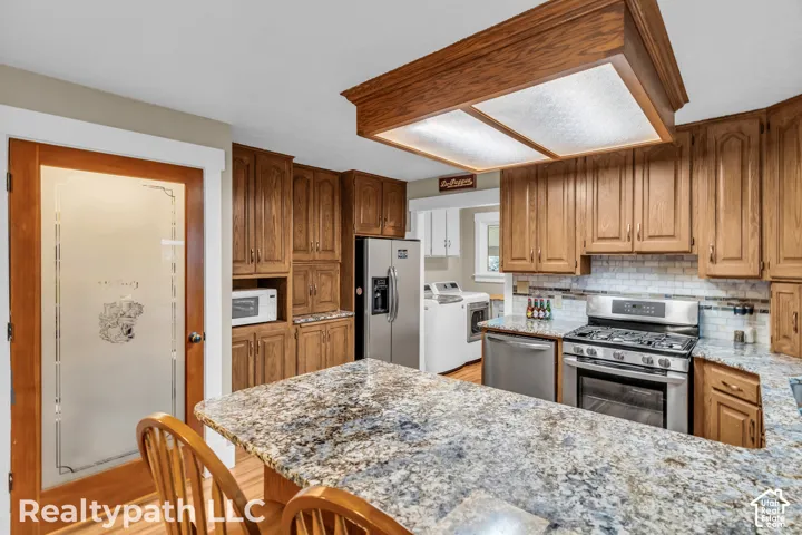Kitchen featuring wood cabinetry, stainless steel appliances, a tile backsplash, and stone countertops