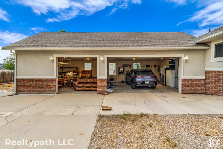 Two-car garage featuring a concrete driveway, brick wainscoting, stucco siding, dual outdoor wall sconces, and a composition shingle roof