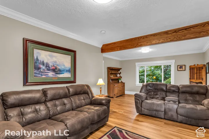Living area featuring wood-finish flooring, a decorative exposed beam, and crown molding