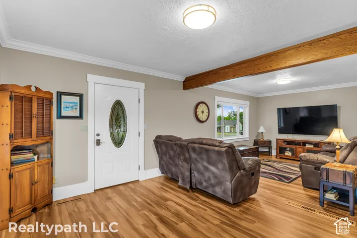Spacious living area featuring wood-finish flooring, a white paneled entry door with decorative glass, and a prominent wood ceiling beam
