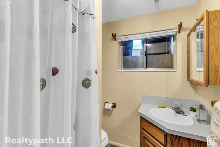 Bathroom featuring a corner vanity with wood-finish cabinetry, a built-in sink, and a light-colored countertop