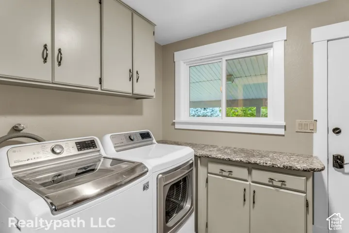 Dedicated laundry space featuring upper and lower cabinetry, a stone-finish countertop, and a sliding window with white trim
