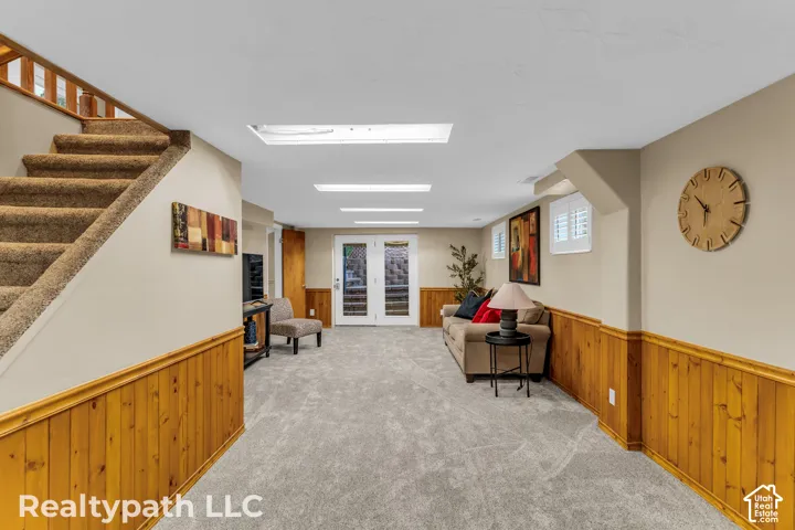 Spacious carpeted room featuring light tan walls, wood paneling, and an exposed wood staircase with carpeted treads