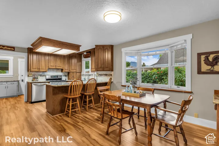 Kitchen featuring wood-finish flooring, rich wood cabinetry, stainless steel appliances, and granite countertops