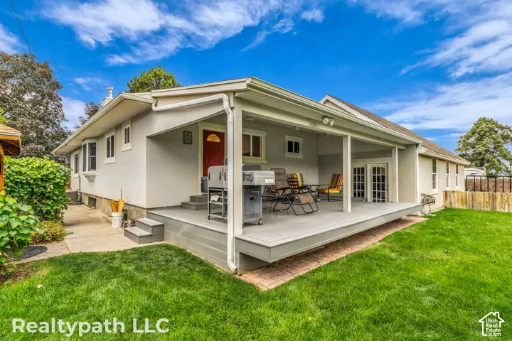 Spacious backyard featuring a covered patio with composite decking, French doors, and mature landscaping